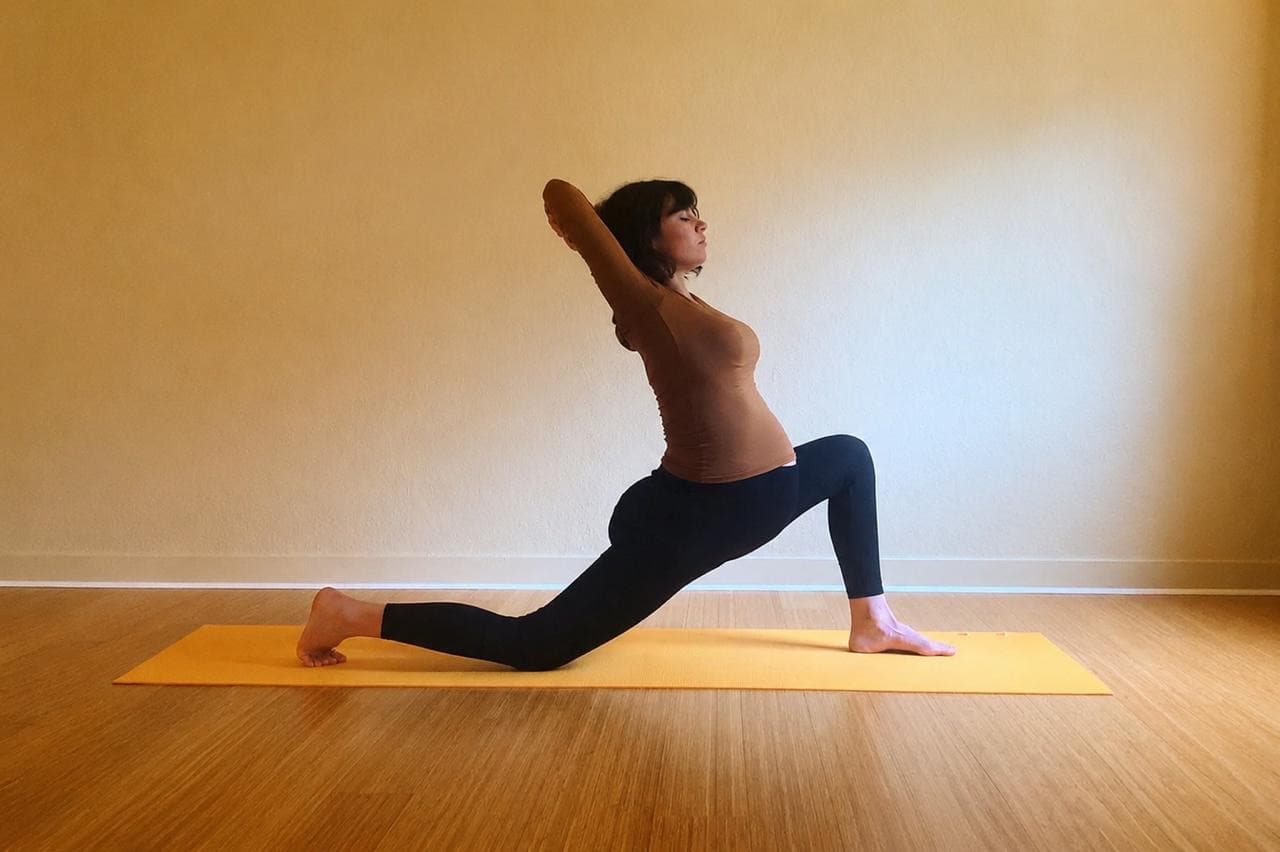 Femme enceinte en fente basse, bras levés, sur un tapis orange